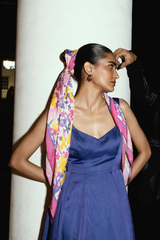 Woman wearing a colorful scarf with blue dress standing against a white column